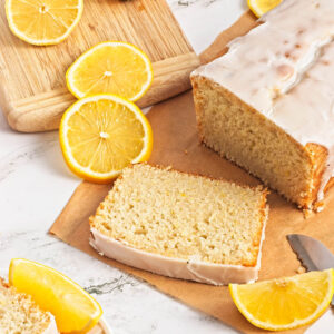 Lemon loaf cake on parchment paper with lemon pieces scattered on wood cutting board.