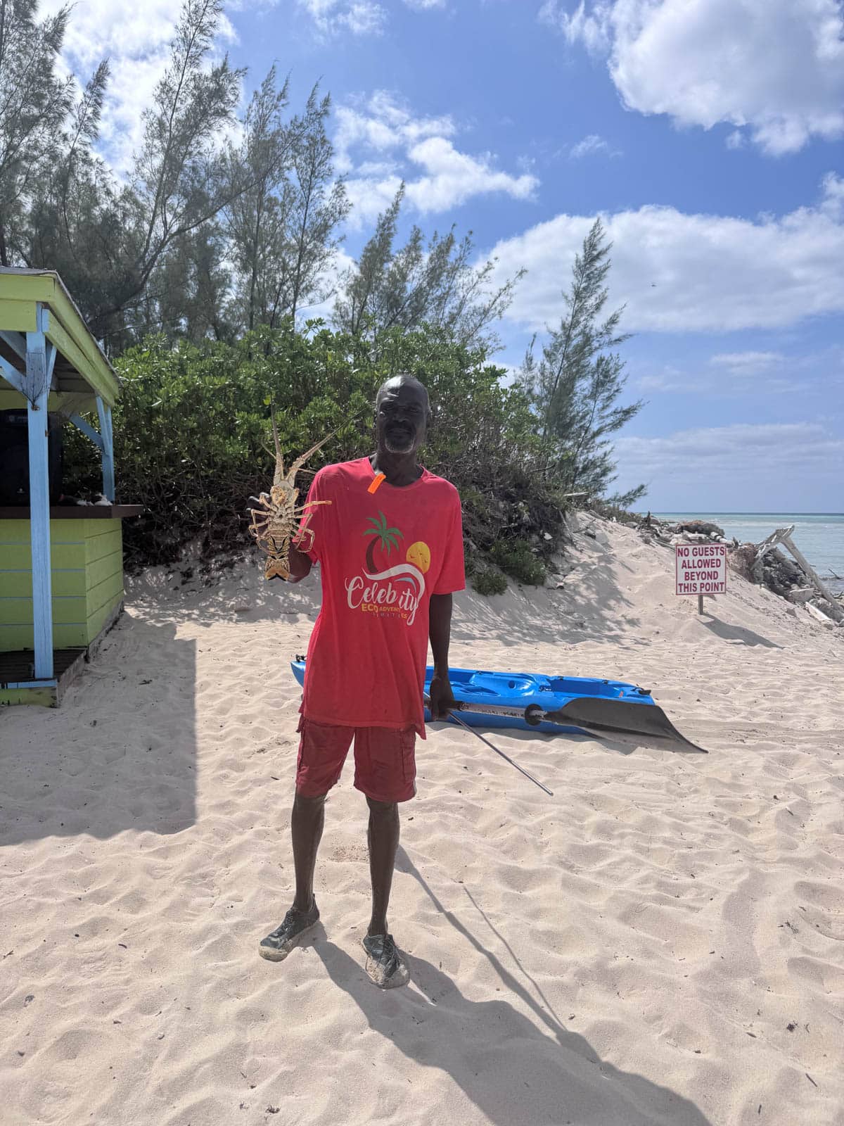 Man holding lobster on beach.