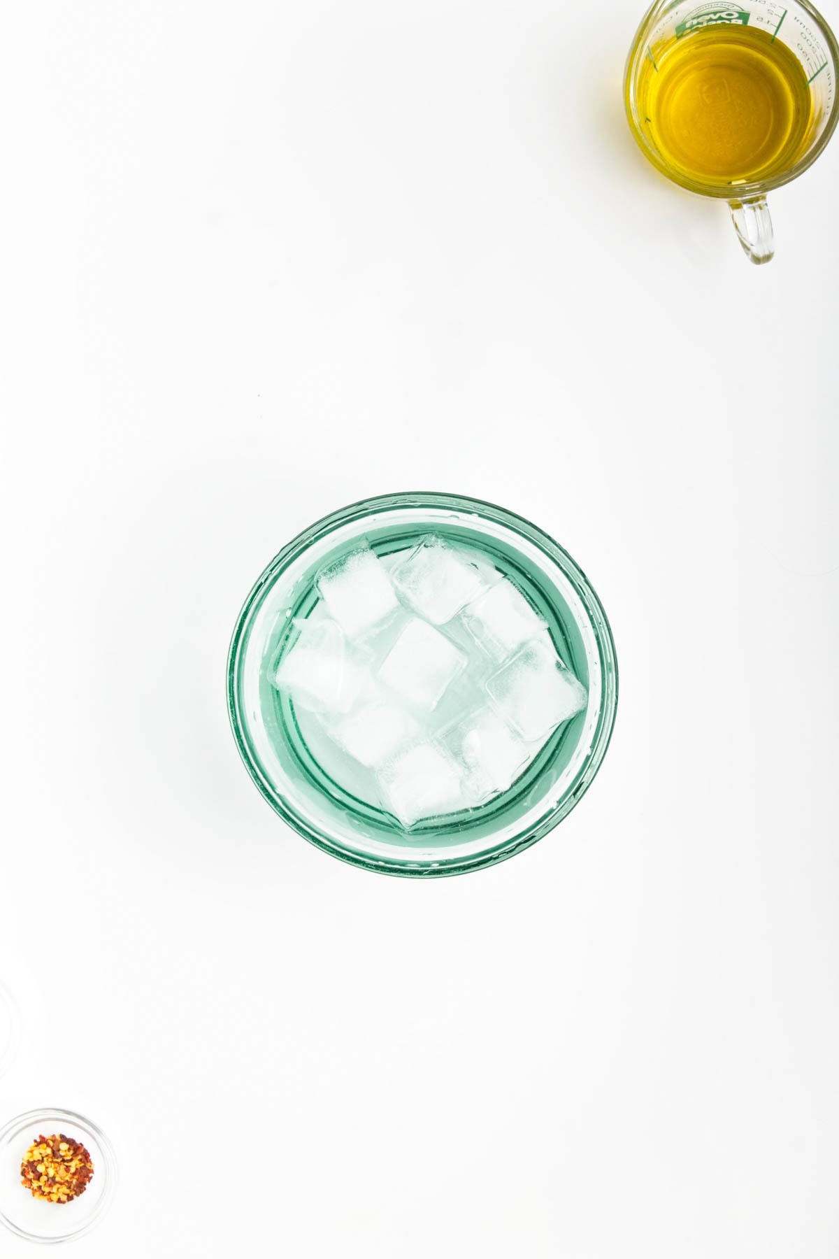 Glass bowl with ice cubes, red pepper flakes in a small bowl, olive oil in a glass measuring cup.