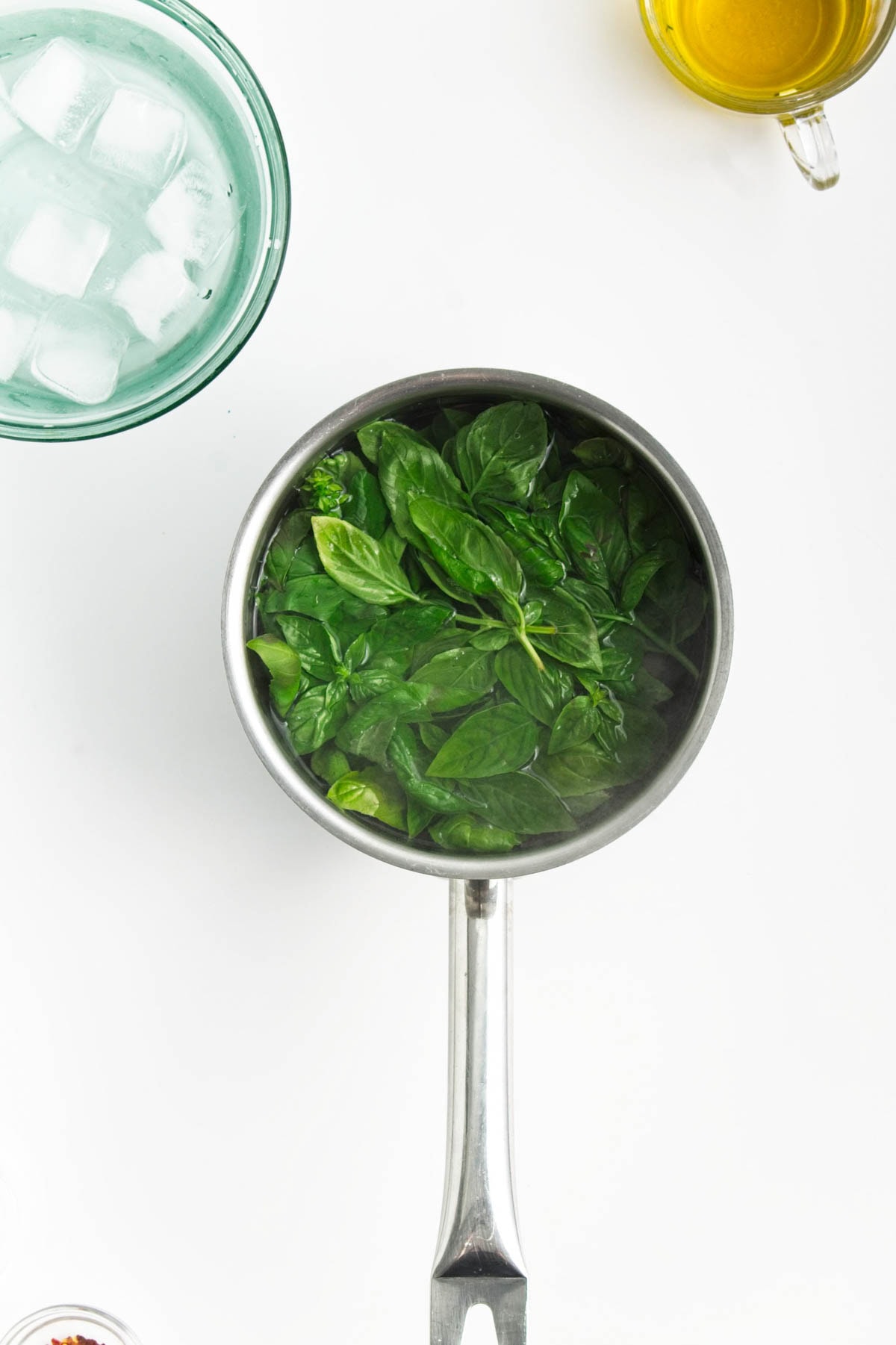 Basil in water in sauce pan with bowl of ice and cup of olice oil.