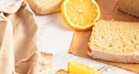 Lemon loaf cake on parchment paper with lemon pieces scattered on wood cutting board.