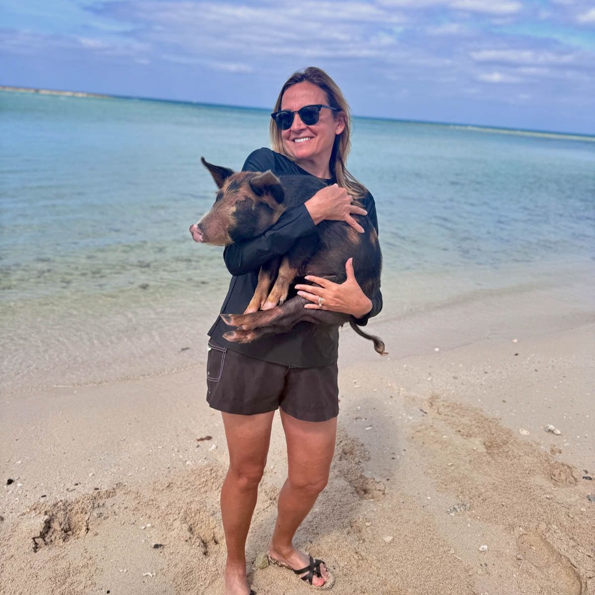Woman on beach holiding a small pig.