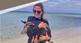 Woman holding pig on beach.