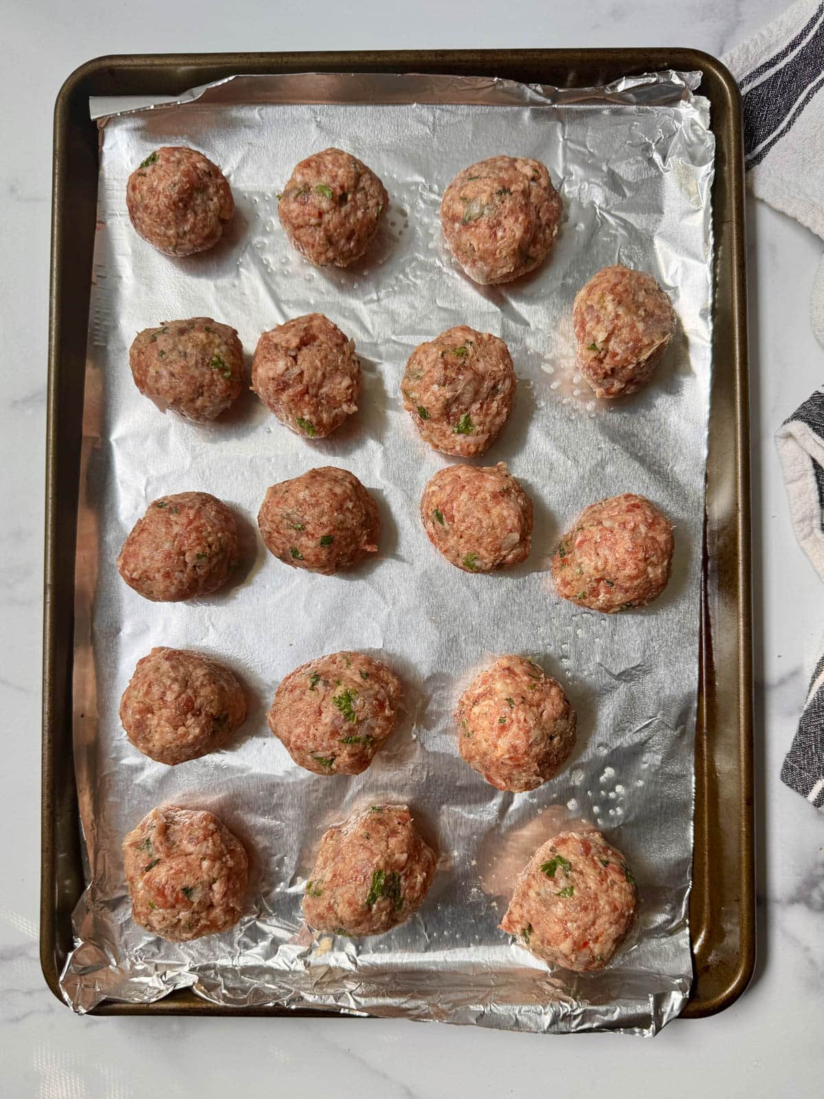 Raw meatballs on a foil-lined baking sheet.