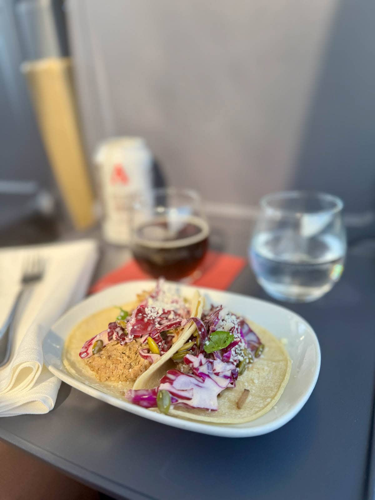 Tacos with shredded pork and red cabbage, with glasses of brown liquid and water in the background.