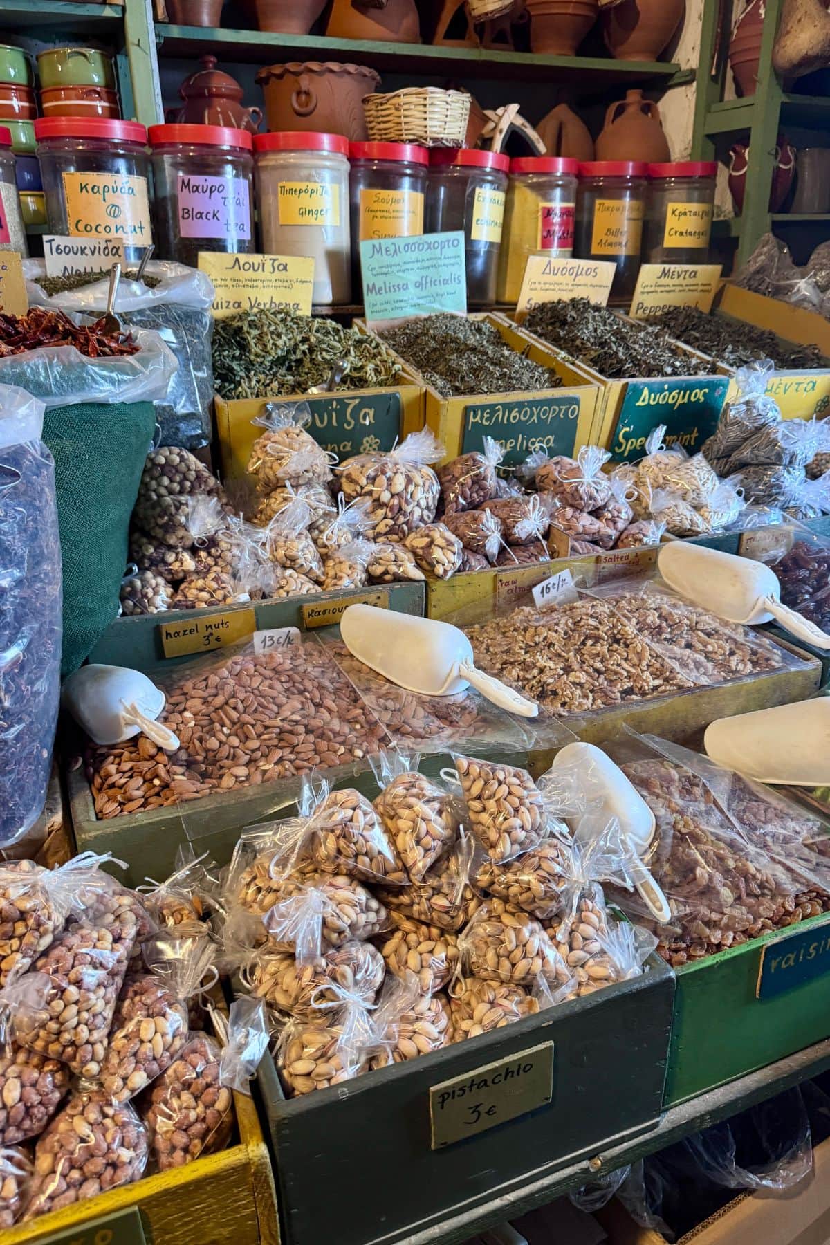 Greek nuts and spices in a store in Greece with containers and crocks on shelves above.