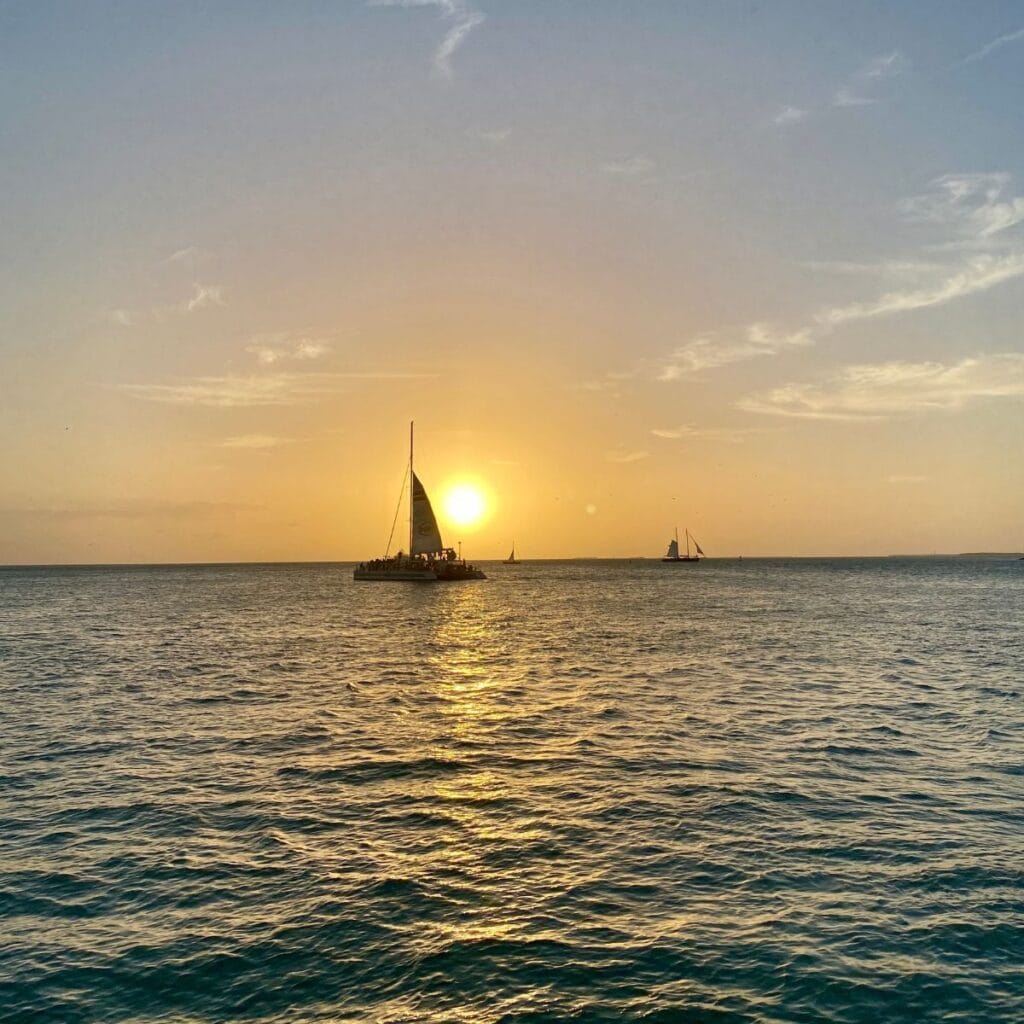Sailboat on water in front of setting sun.