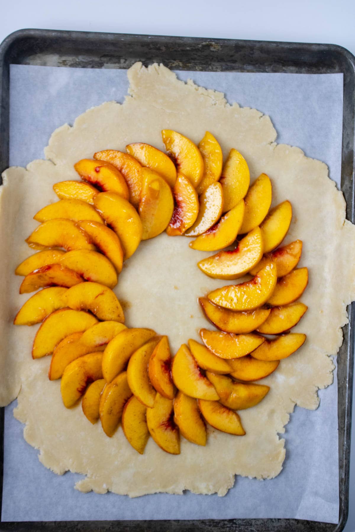Pie crust rolled out and set on parchment paper on baking sheet topped with sliced peaches.