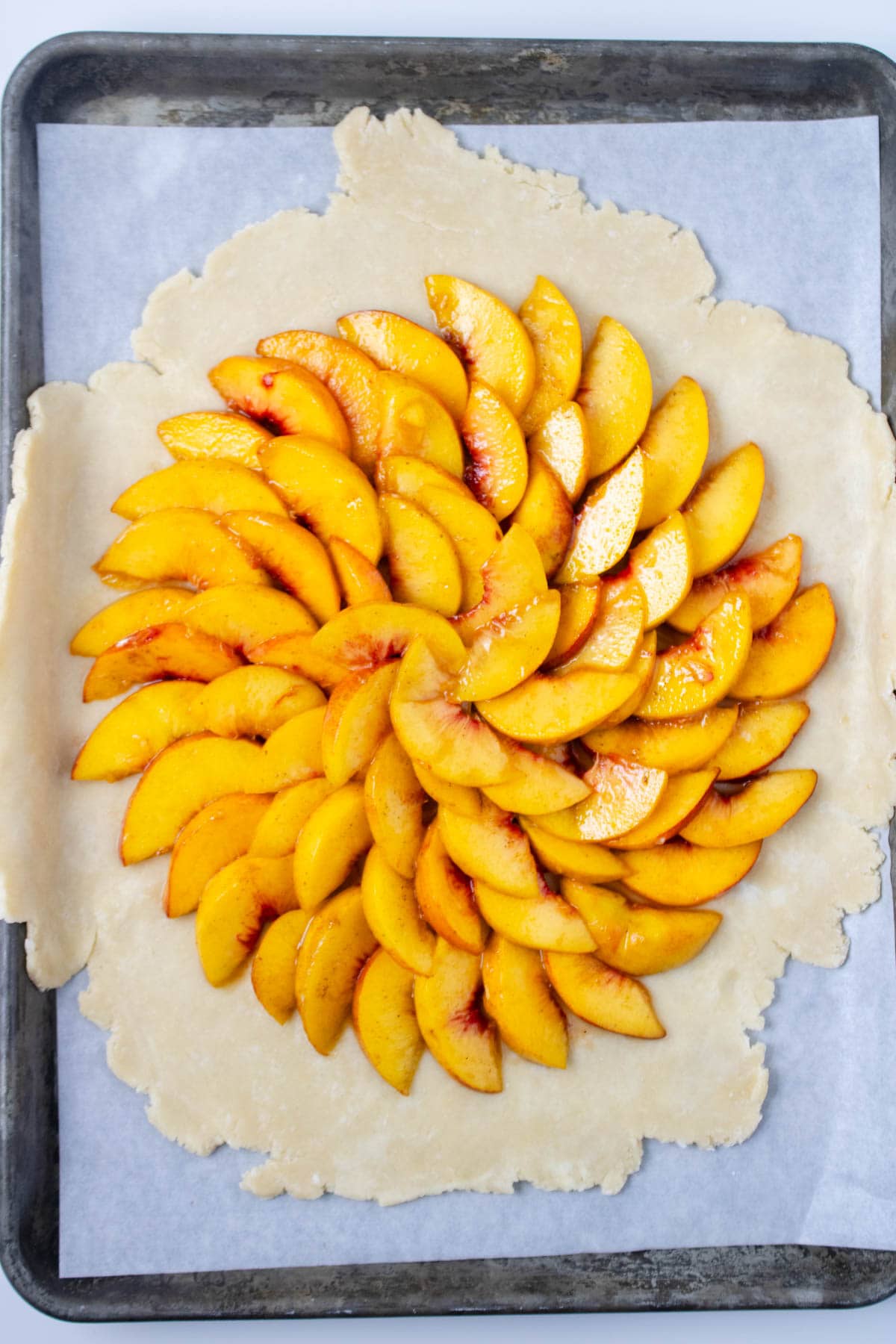 Pie crust rolled out and set on parchment paper on baking sheet almost covered with sliced peaches.