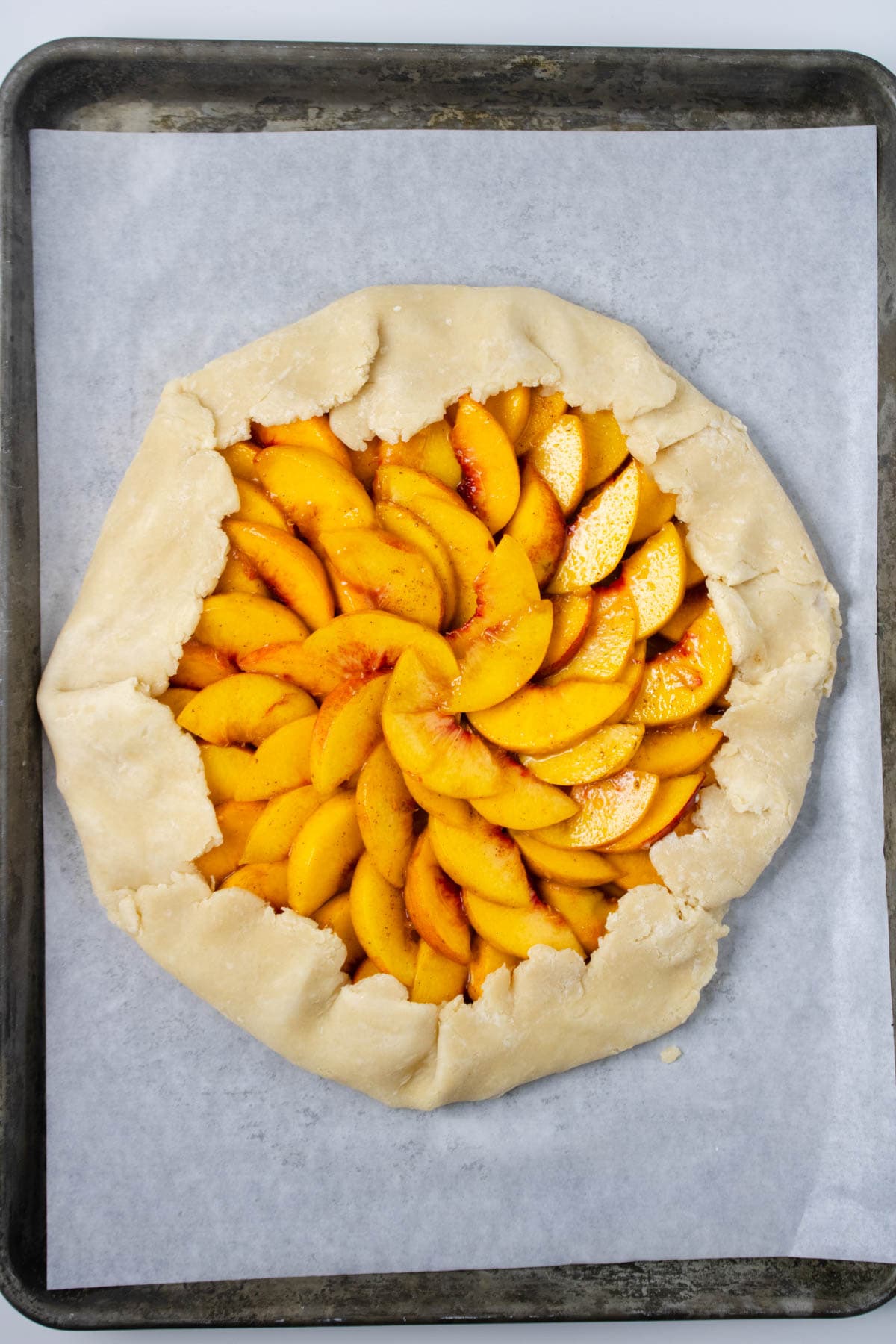 Pie crust rolled out and set on parchment paper on baking sheet topped with sliced peaches with ends of crust folded over fruit.