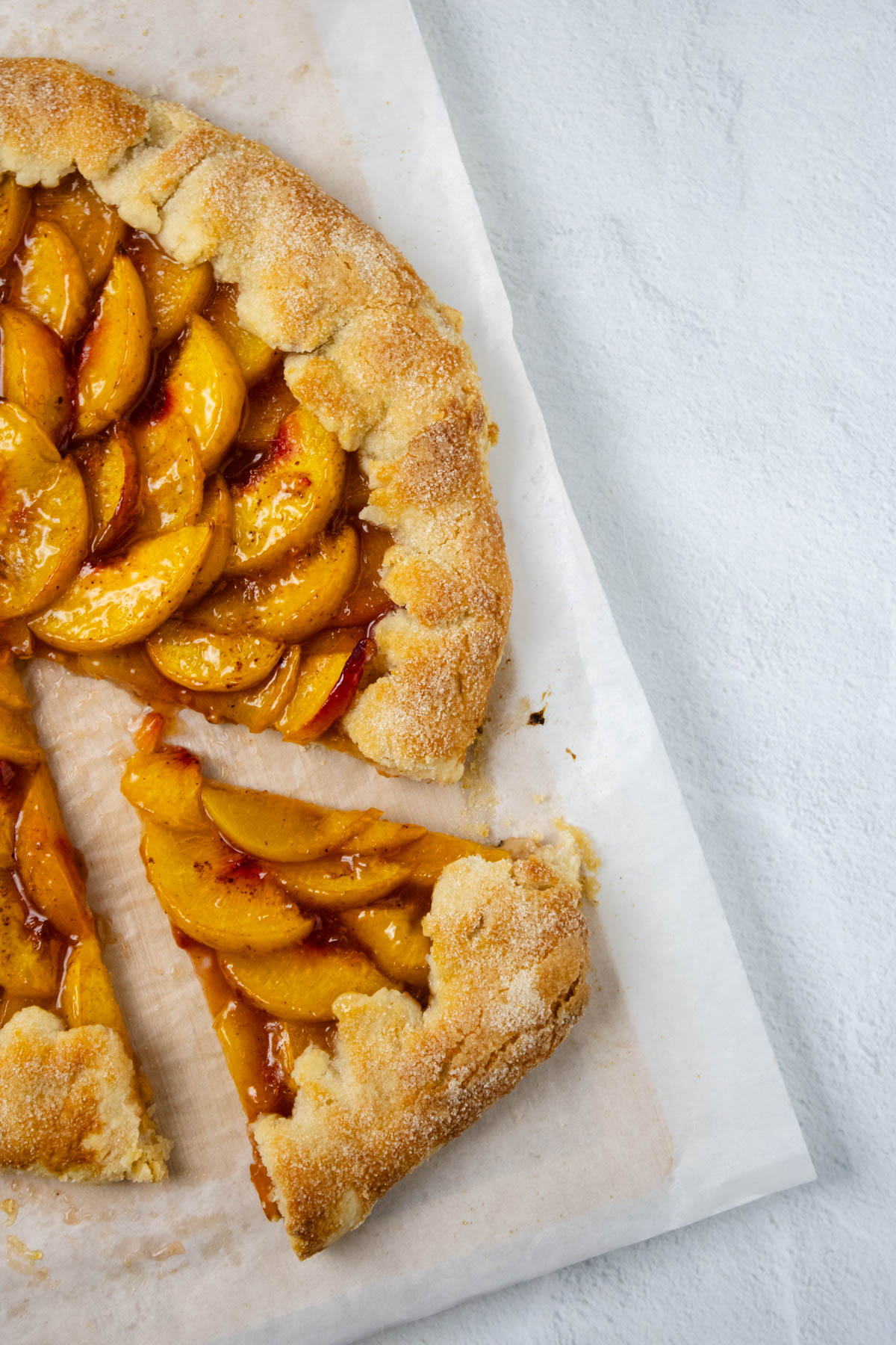 Part of a baked peach galette on parchment paper with one slice pulled out.