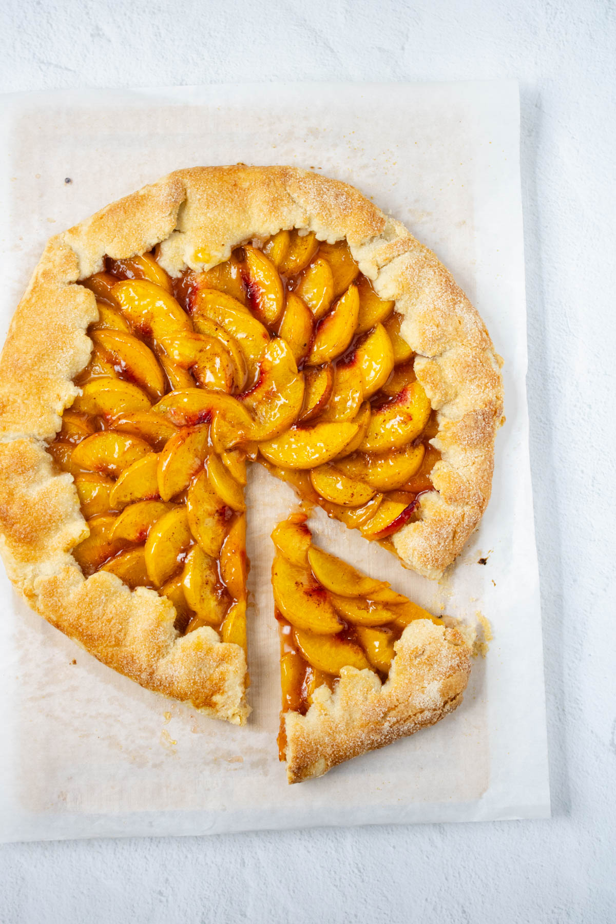 Peach tart on parchement paper with slice cut and slid out slightly.