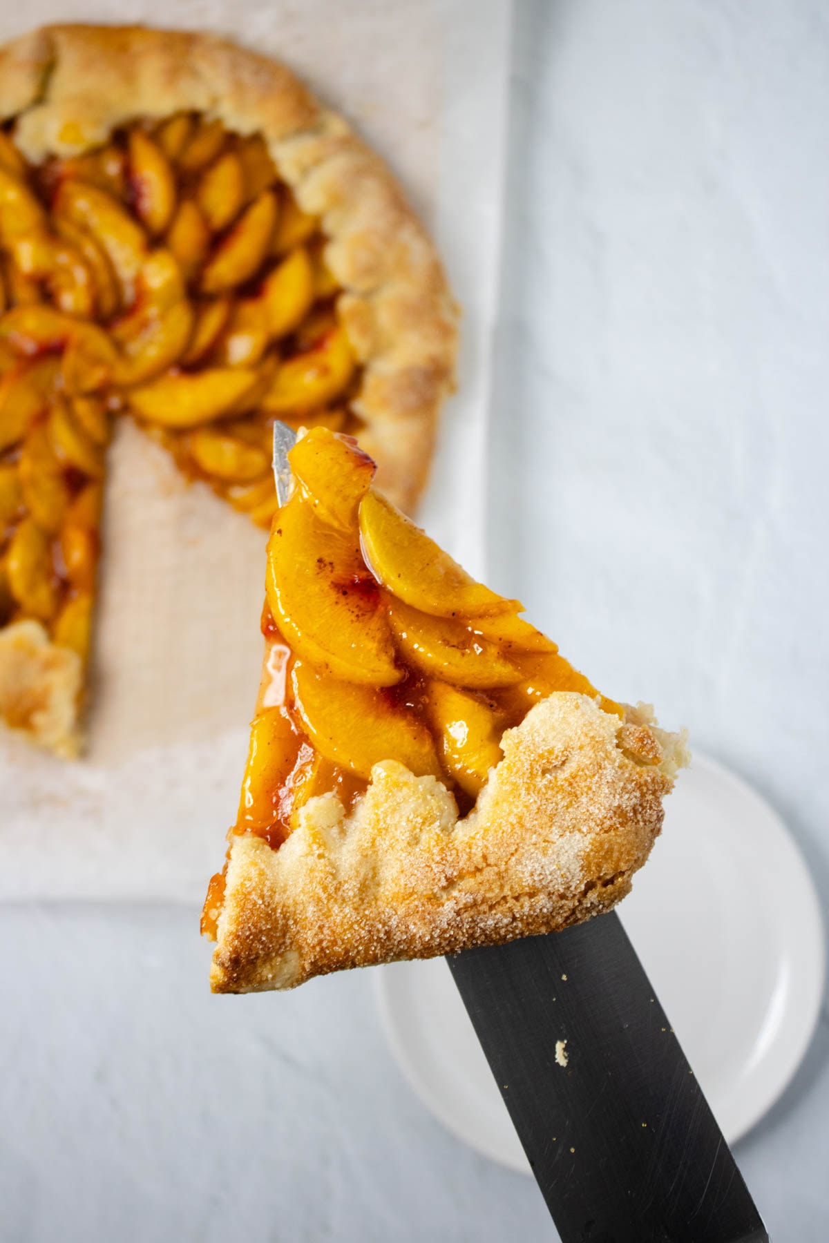 Peach galette with slice held up on spatula and rest of pie below.