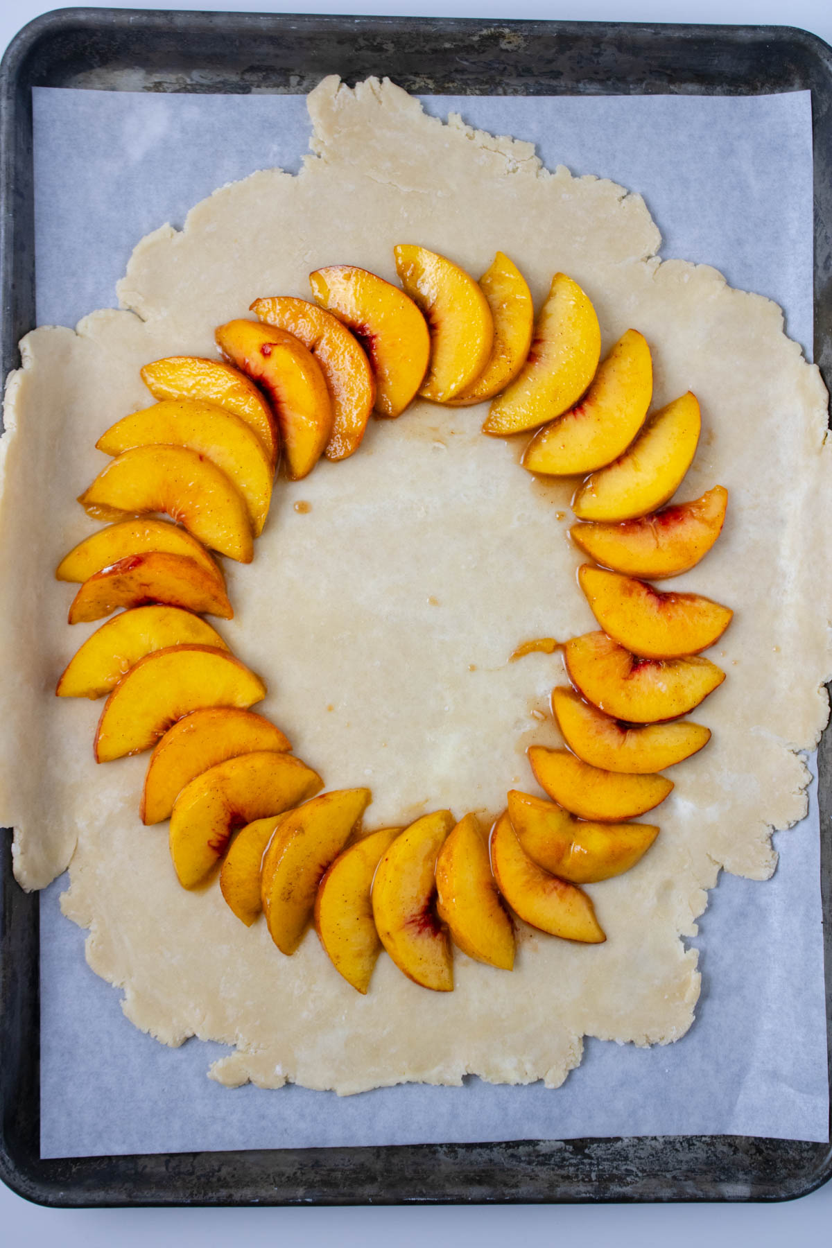 Pie crust rolled out and set on parchment paper on baking sheet topped with sliced peaches.