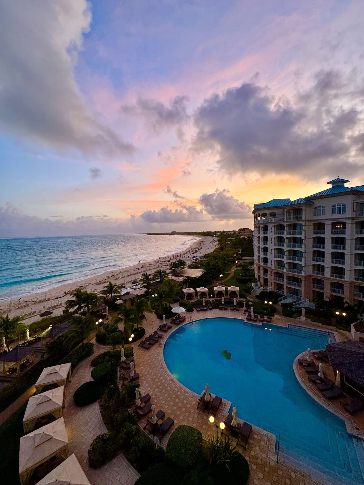 Sunrise in the distance beyond a resort, pool, and bay.