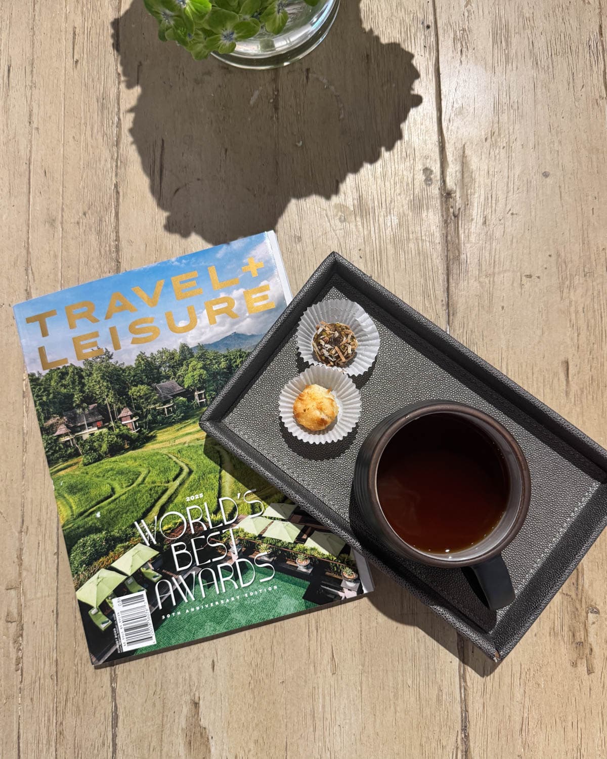 Magazine on table with a cup of tea and two treats on tray.