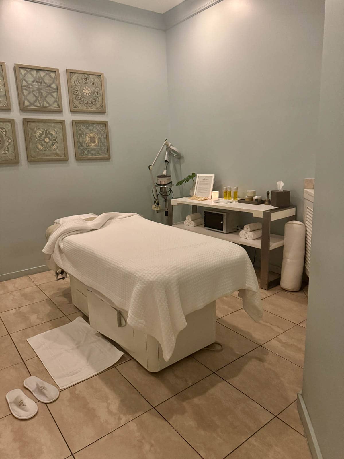 Spa bed with towel and slippers on floor.