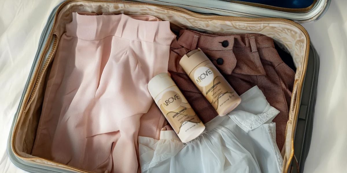 Suitcase open withh clothing and bottles of shampoo and conditioner.