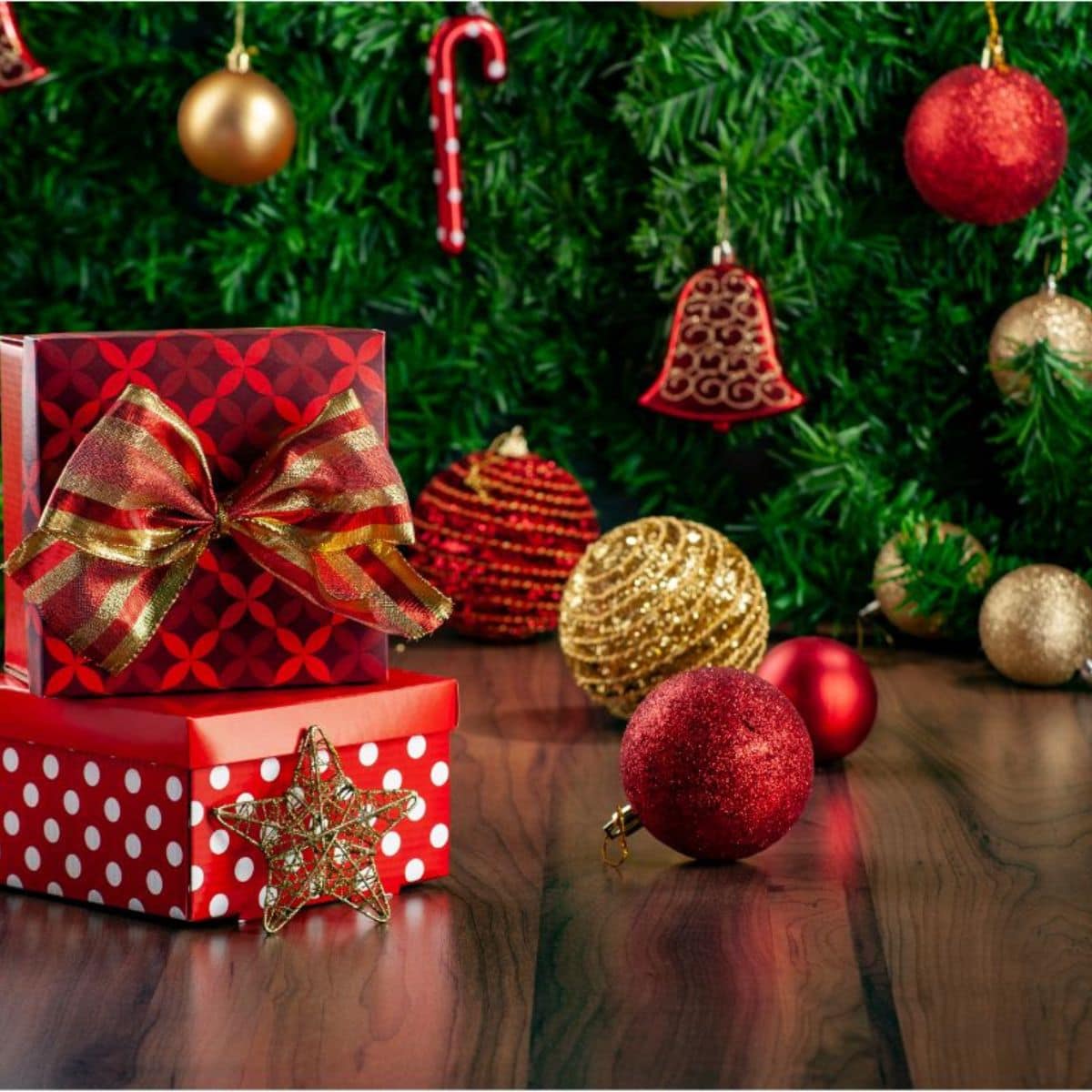 Holiday gifts wrapped in red and gold paper with Christmas tree and ornaments in background.