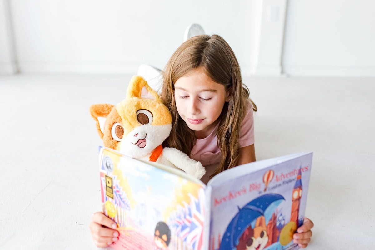 Young girl on floor holiding cat plush and reading a book.