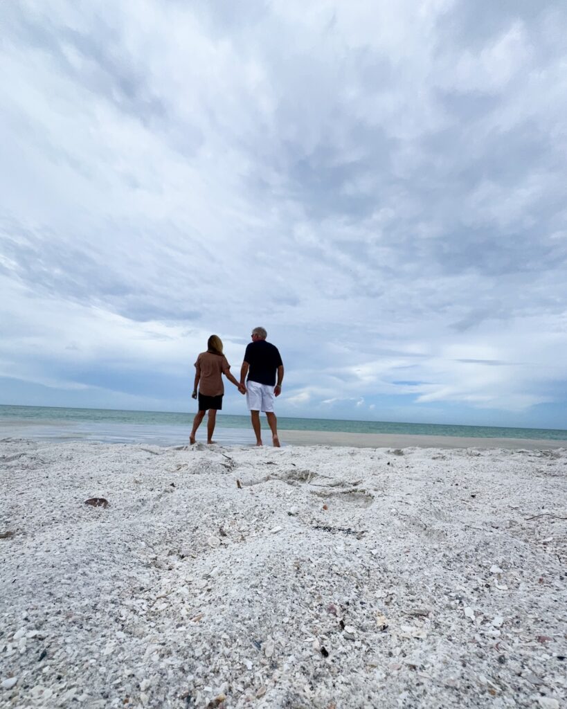 Man and woman holding hands on beach.