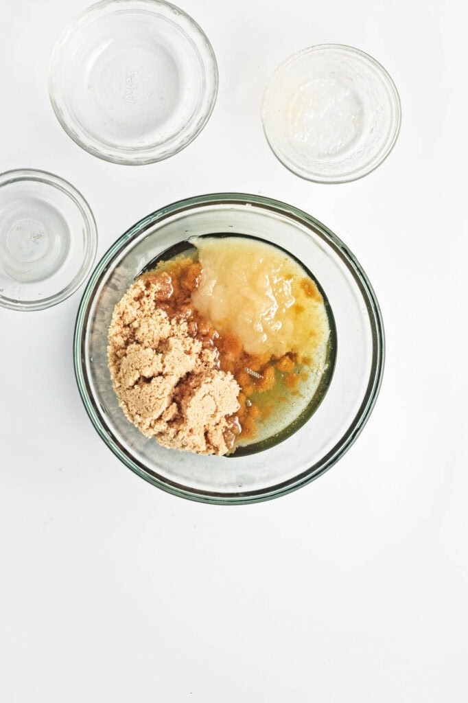 Applesauce, vegetable oil, brown sugar, and vanilla in a glass bowl.