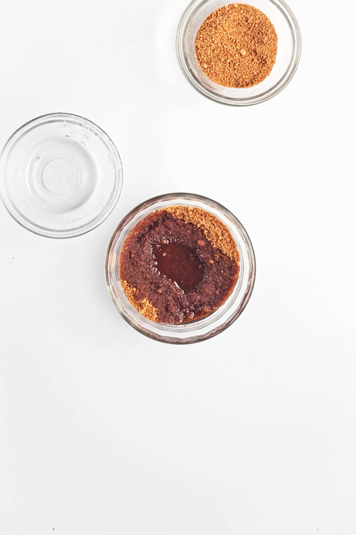 Spices with coconut oil in a glass bowl, an empty glass bowl, and more dry spices in another glass bowl.