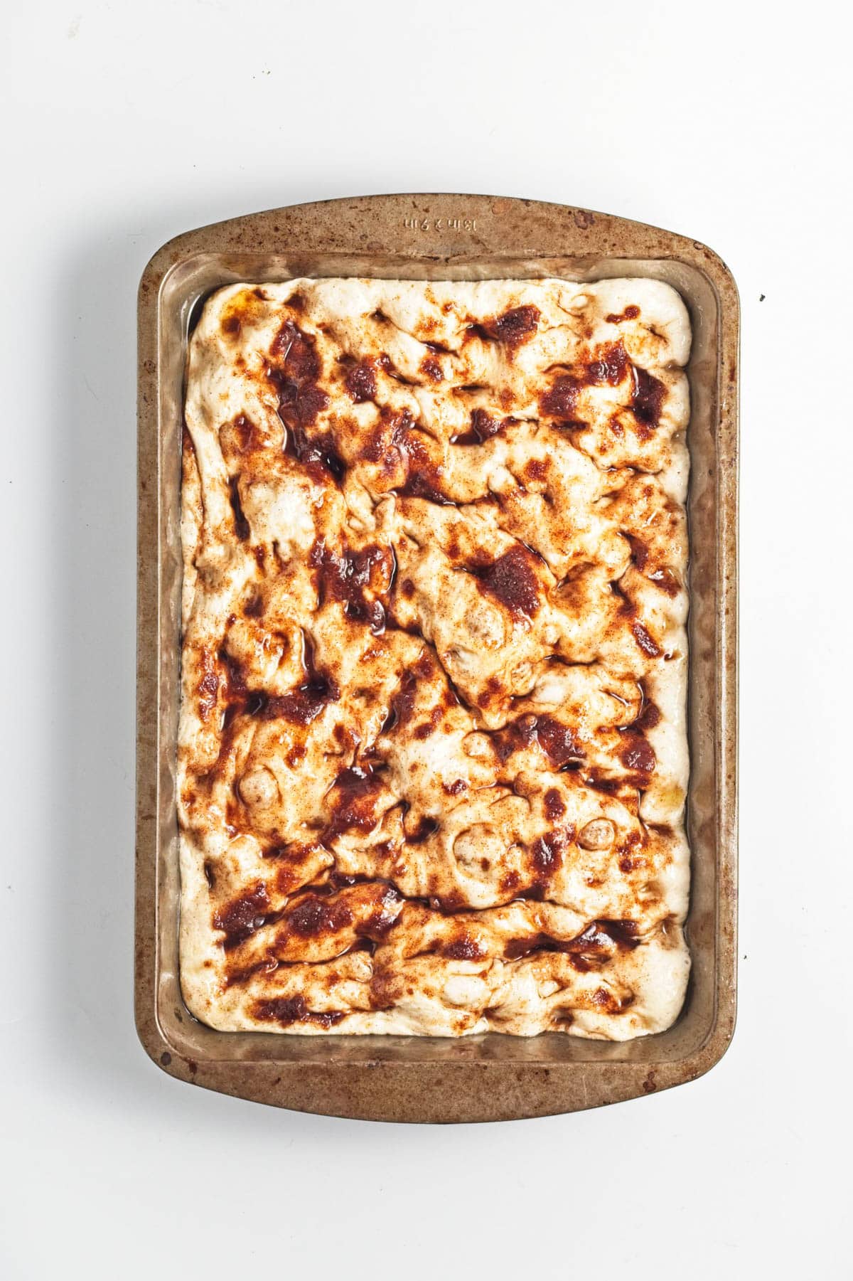 Dough topped with spice paste in a baking pan.