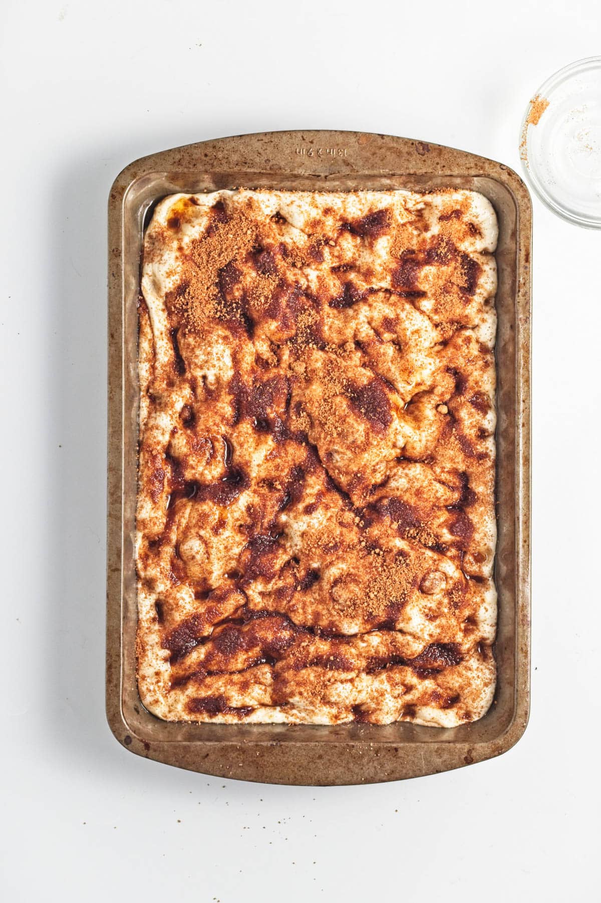 Dough topped with spices in a baking pan.