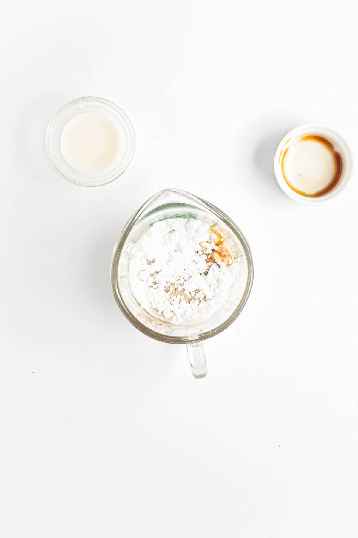 Powdered sugar, vanilla, and milk in a measuring cups with empty bowls.