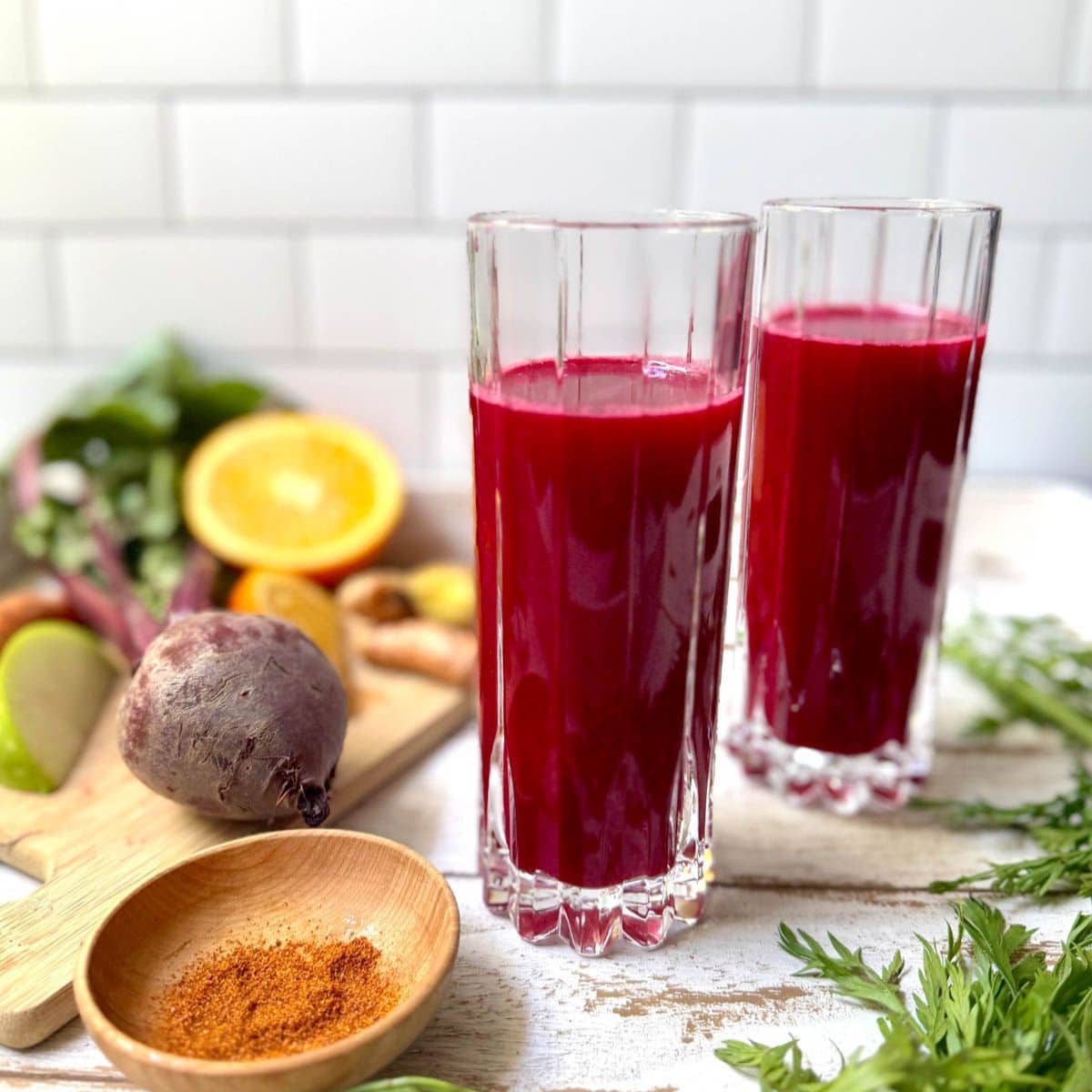 Glasses of fruit and vegetable juice with fruits and vegetables in background and bowl of cayenne pepper.
