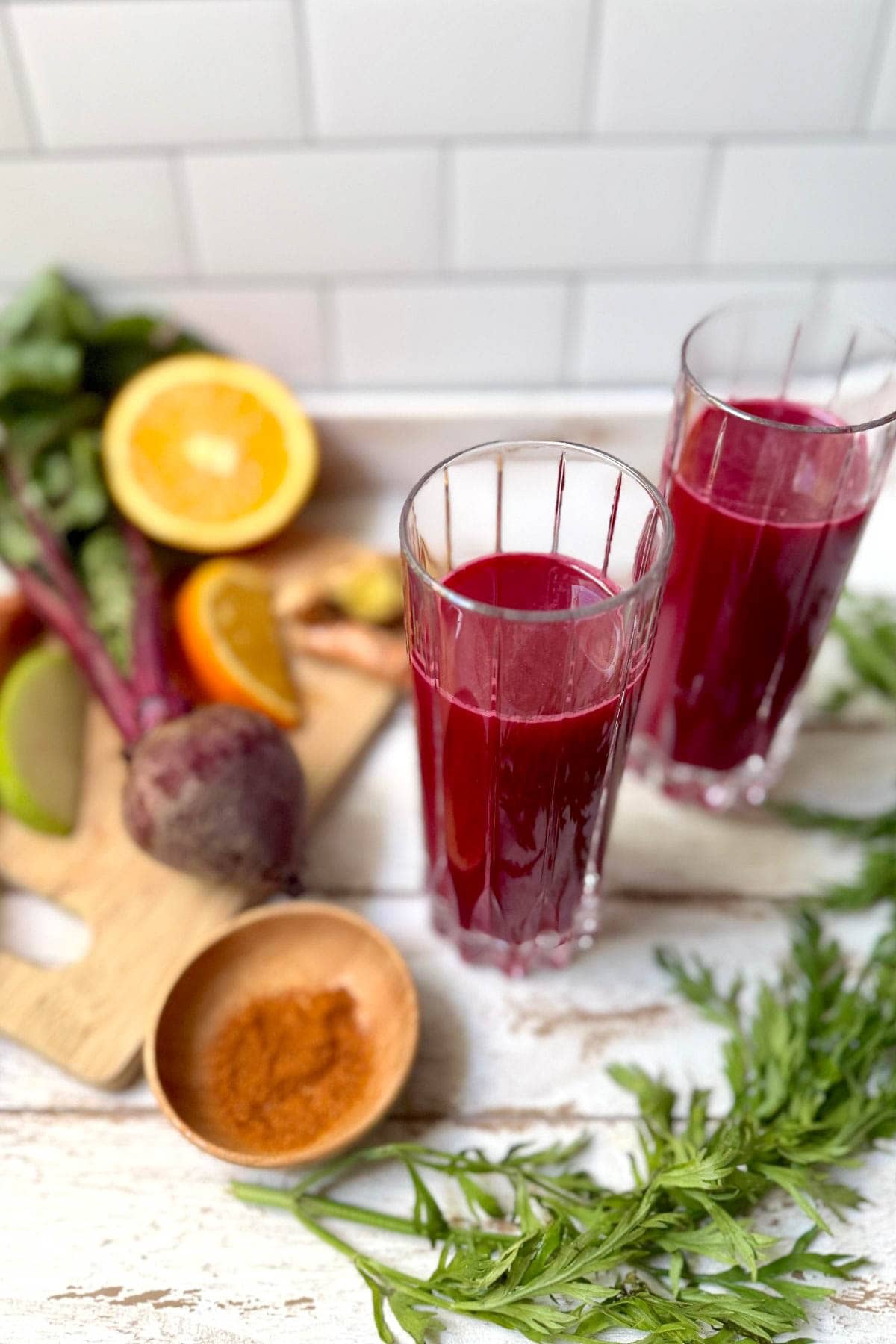 Glasses of fruit and vegetable juice with fruits and vegetables in background and bowl of cayenne pepper.