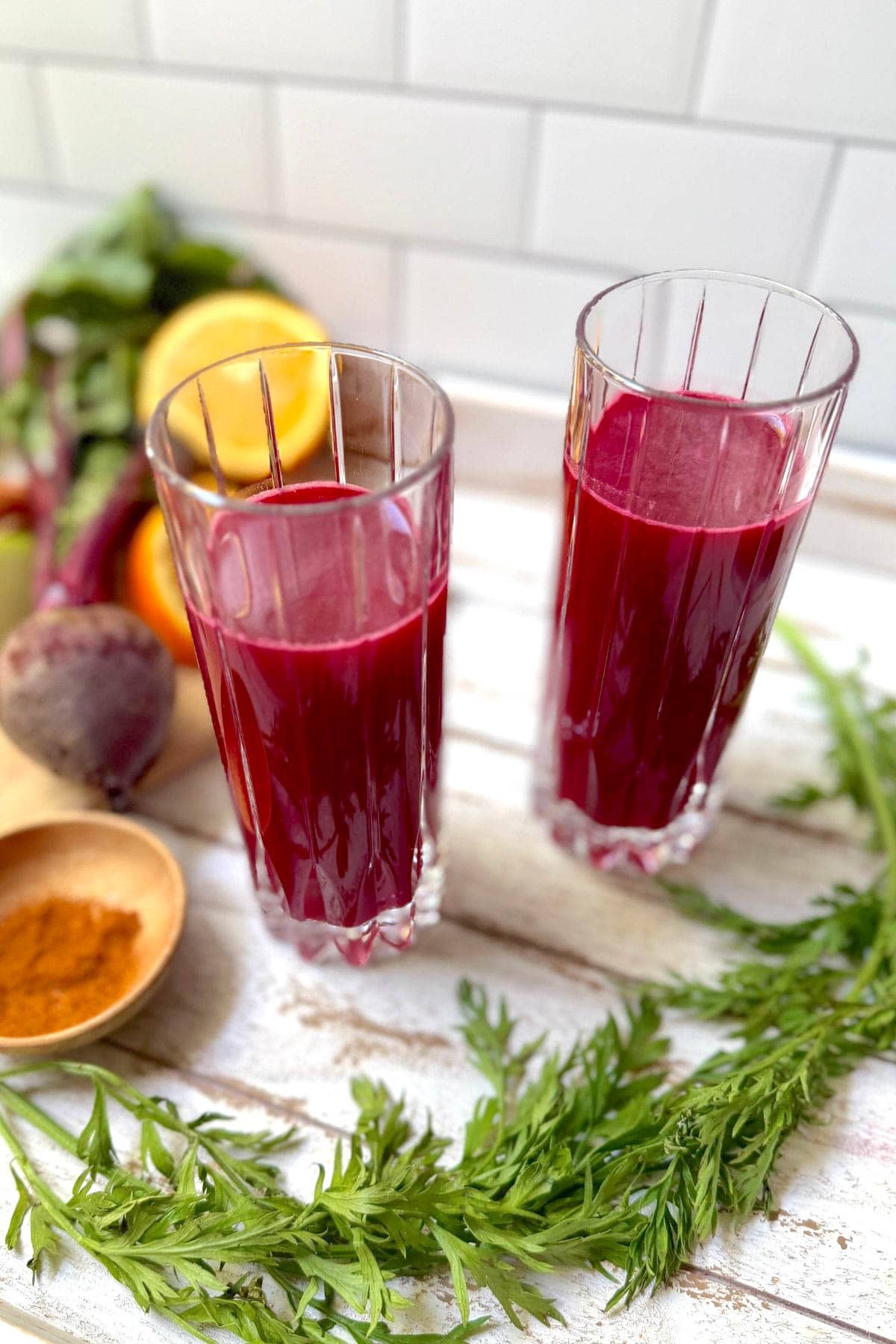 Glasses of fruit and vegetable juice with fruits and vegetables in background and bowl of cayenne pepper.