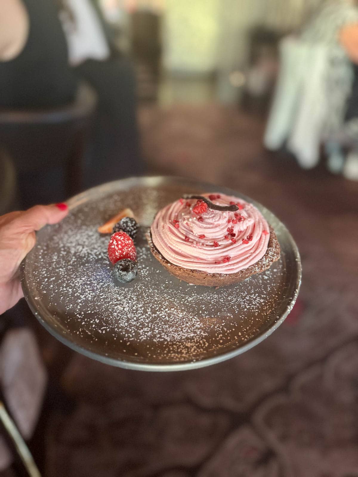 Chocolate dessert with cherry frosting on a gray plate with powdered sugar and berries.