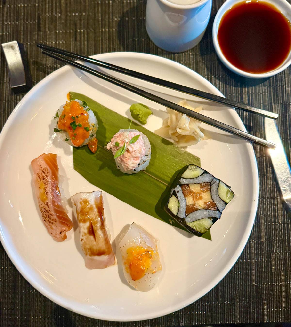 Sushi on a white plate with chopsticks and bowl of soy sauce.