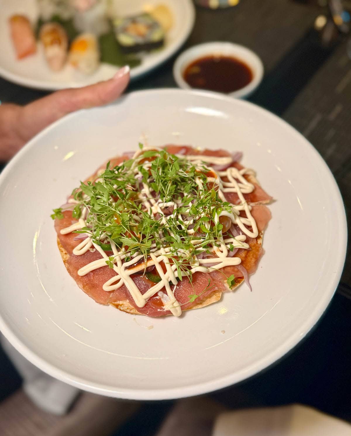 Sliced raw fish on a tortilla with sauce and sprouts.