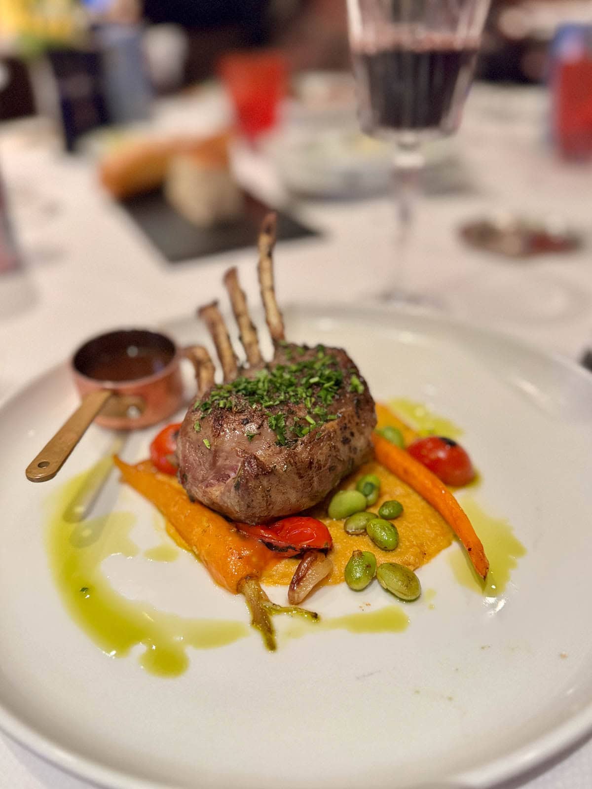 Lamb over orange puree with vegetables on a white plate.