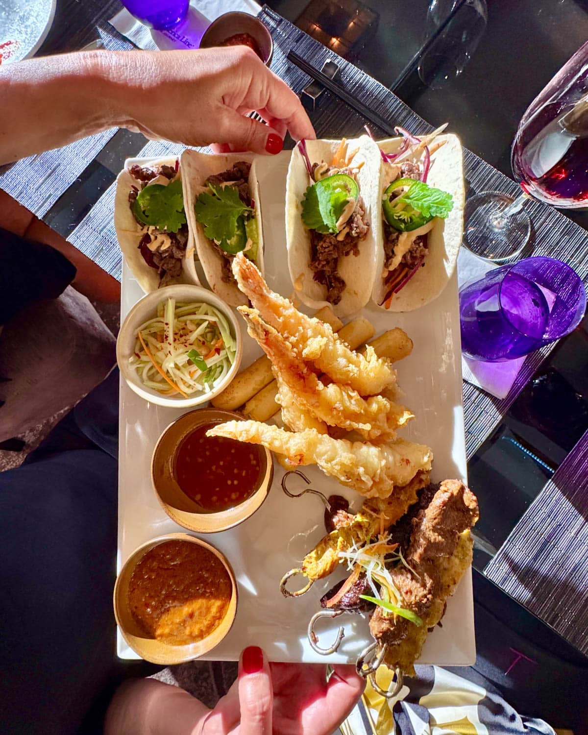 Hands holding a variety of appetizers and sauces on a rectangular plate.