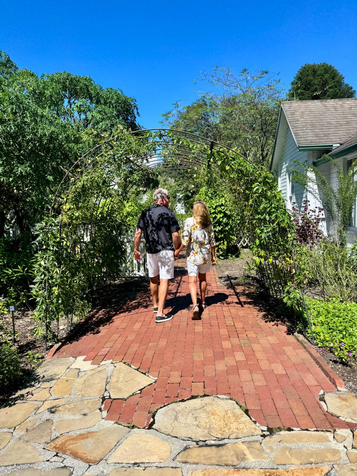 Man and woman walking along a brick path under a trellis.