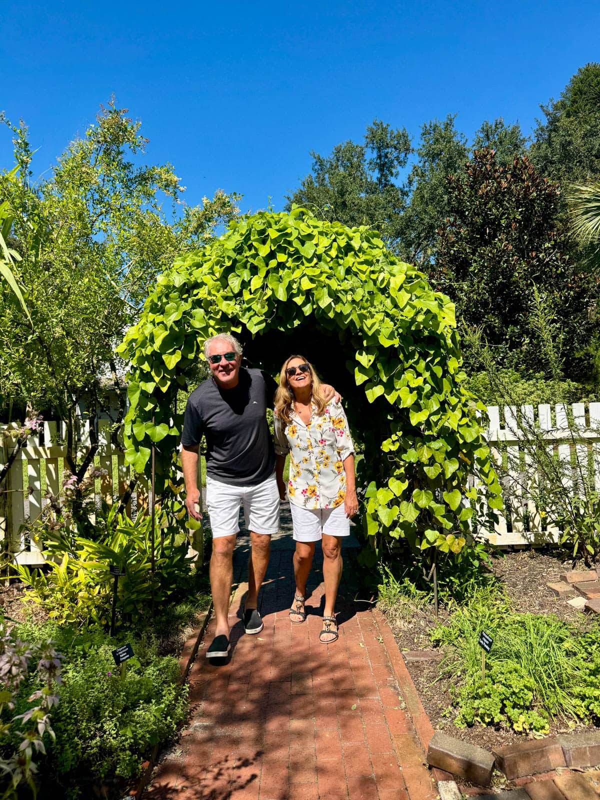 Man and woman walking along a brick path under a trellis.