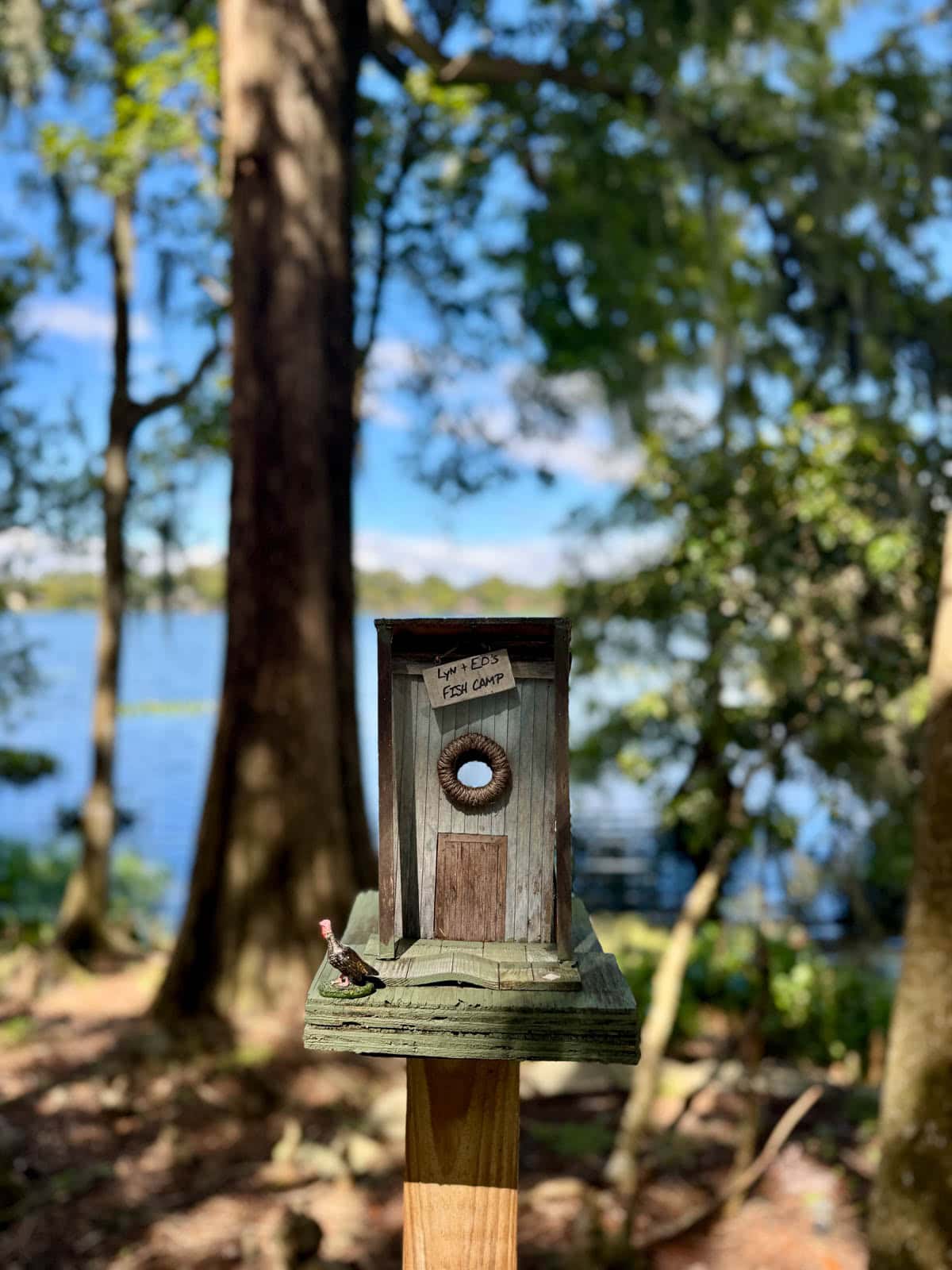 Tiny bird house with trees and a lake in the background.
