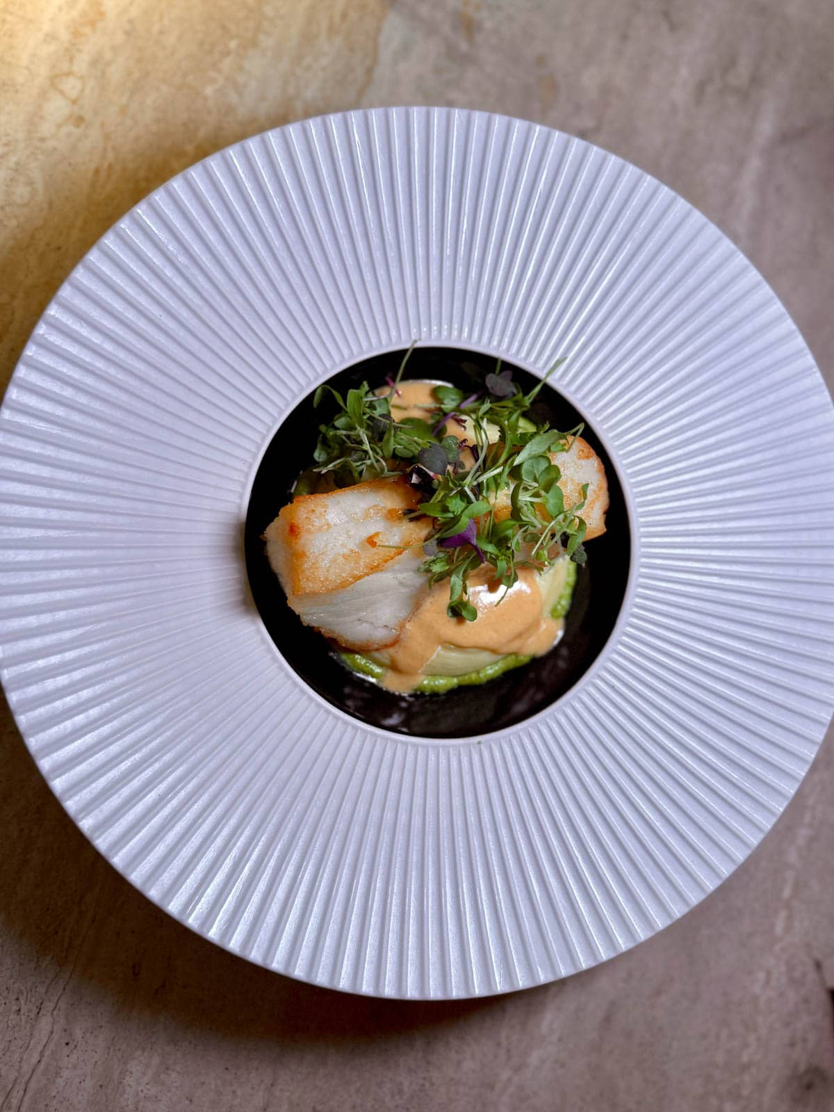 Fish and green sauce topped with herbs in a large-rimmed white bowl.