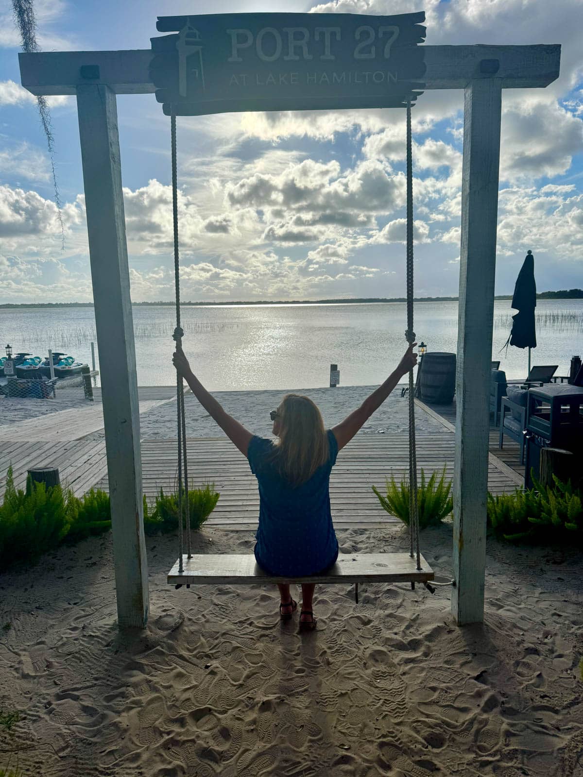 Woman sitting on a swing in front of a boardwalk at a lake.
