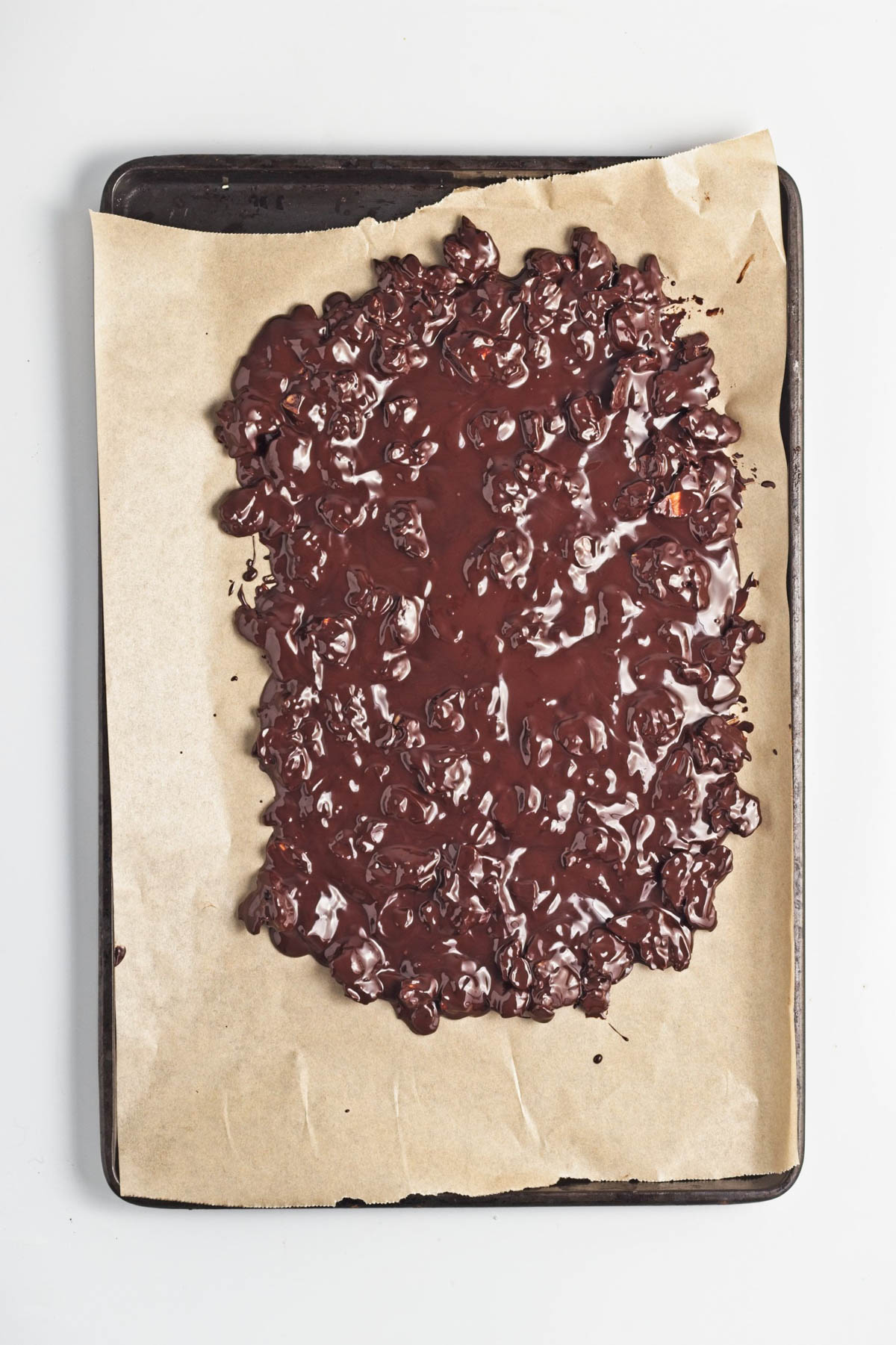Melted dark chocolate poured over almonds on a parchment-lined baking sheet.