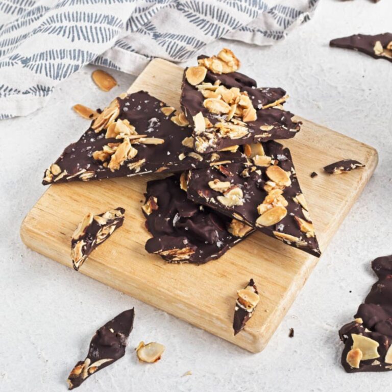 Dark chocolate almond bark on a wood board on a white counter with a dishtowel in the background.