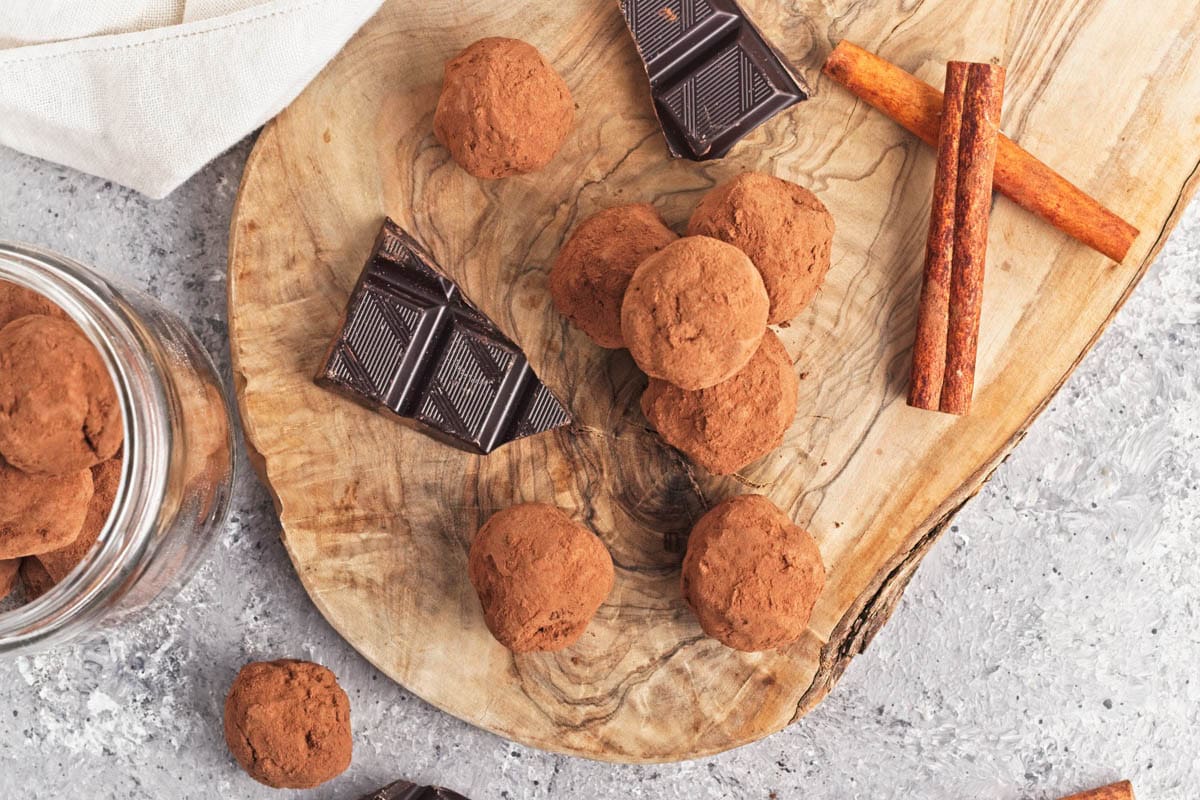 Chocolate truffle balls on a wood cutting board with pieces of chocolate and cinnamon sticks.