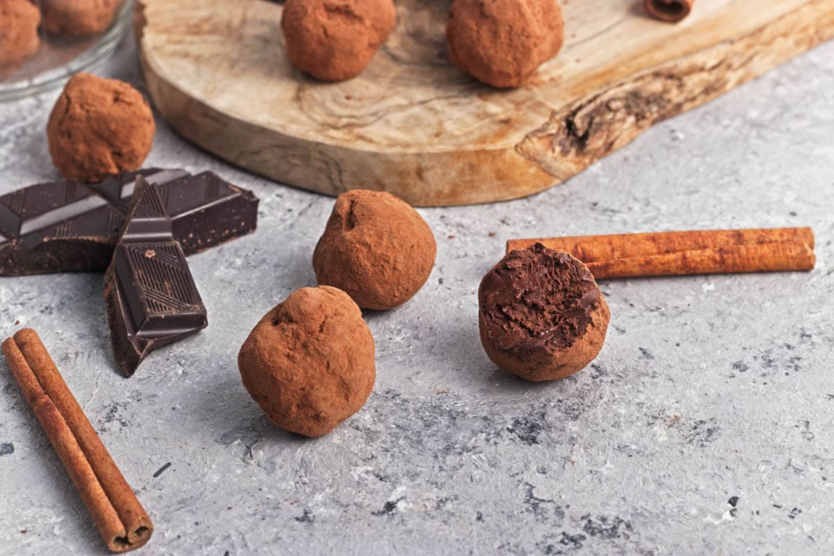 Chocolate truffle balls on a wood cutting board with pieces of chocolate and cinnamon sticks.