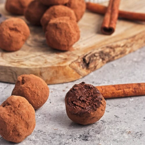 Chocolate truffle balls on a wood cutting board with pieces of chocolate and cinnamon sticks.