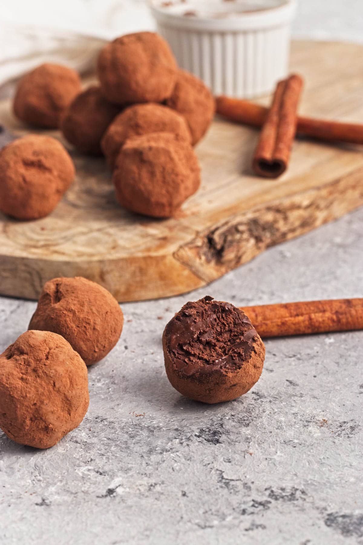 Chocolate truffle balls on a wood cutting board with pieces of chocolate and cinnamon sticks.