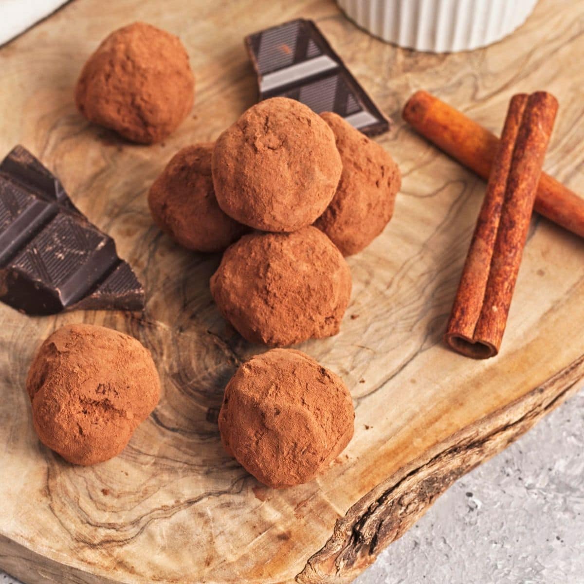 Chocolate truffles and pieces of chocolate and cinnamon sticks on a wood serving board.